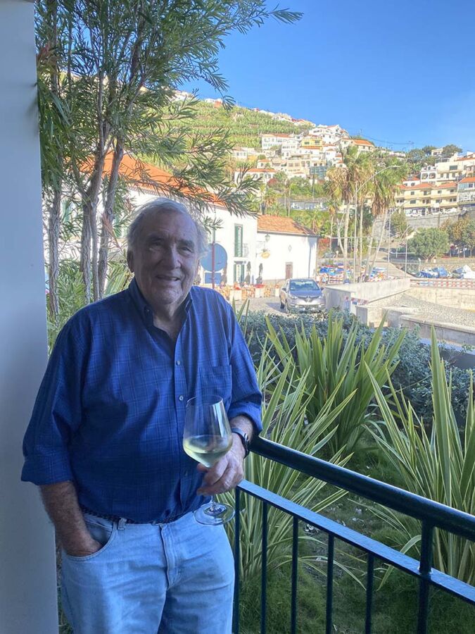 Larry dégustant son vin blanc froid sur son balcon, avec Câmara de Lobos en arrière-plan