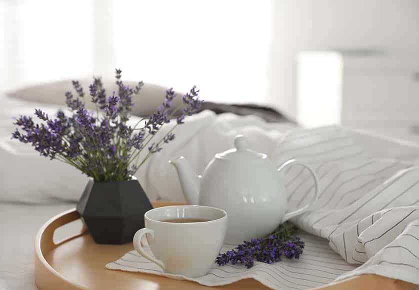 Plateau en bois avec une tasse de thé chaud et de belles fleurs de lavande sur le lit. Petit déjeuner savoureux