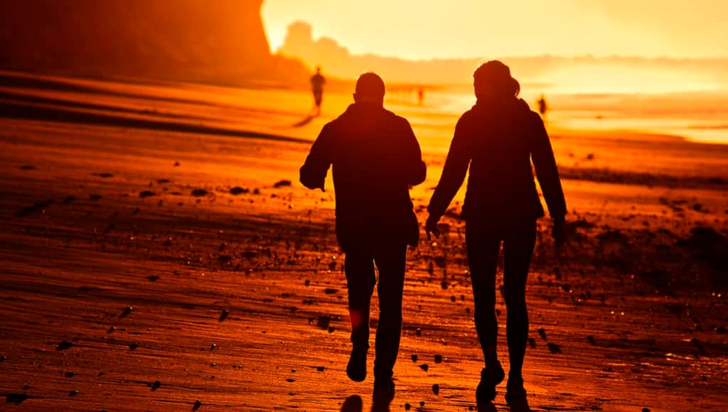 Deux personnes marchant sur la plage de l'Algarve au Portugal tôt le matin, rétroéclairées par le soleil.
